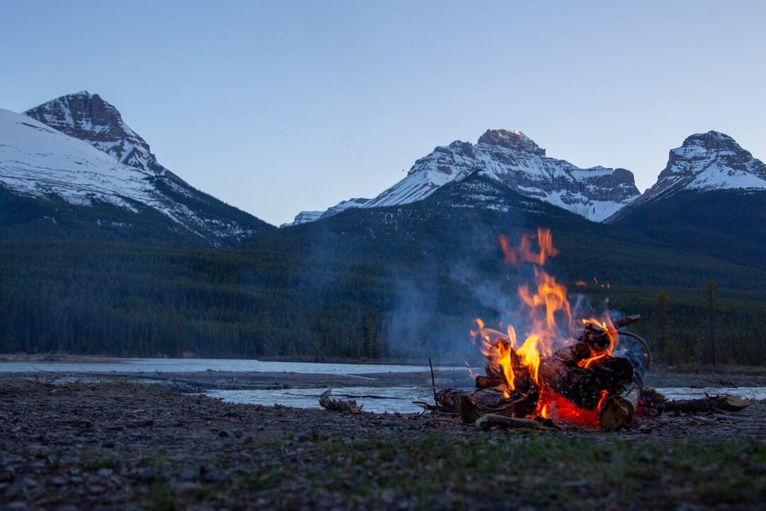 Campfire at dusk with snow-capped mountains